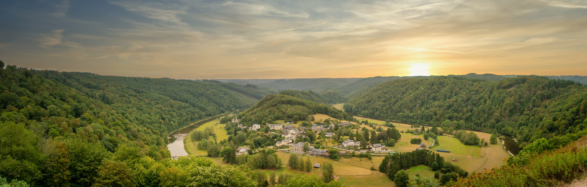 Panorama eines Flusses in einer Hufeisenschleife um ein Dorf, ringsum bewaldete Hänge im Abendlicht